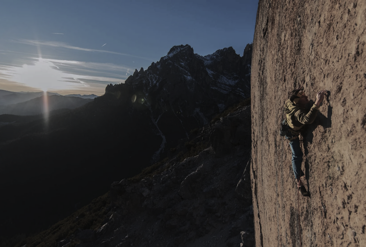 Alessandro Zeni climbing a steep Dolomite rock wall in evening light.